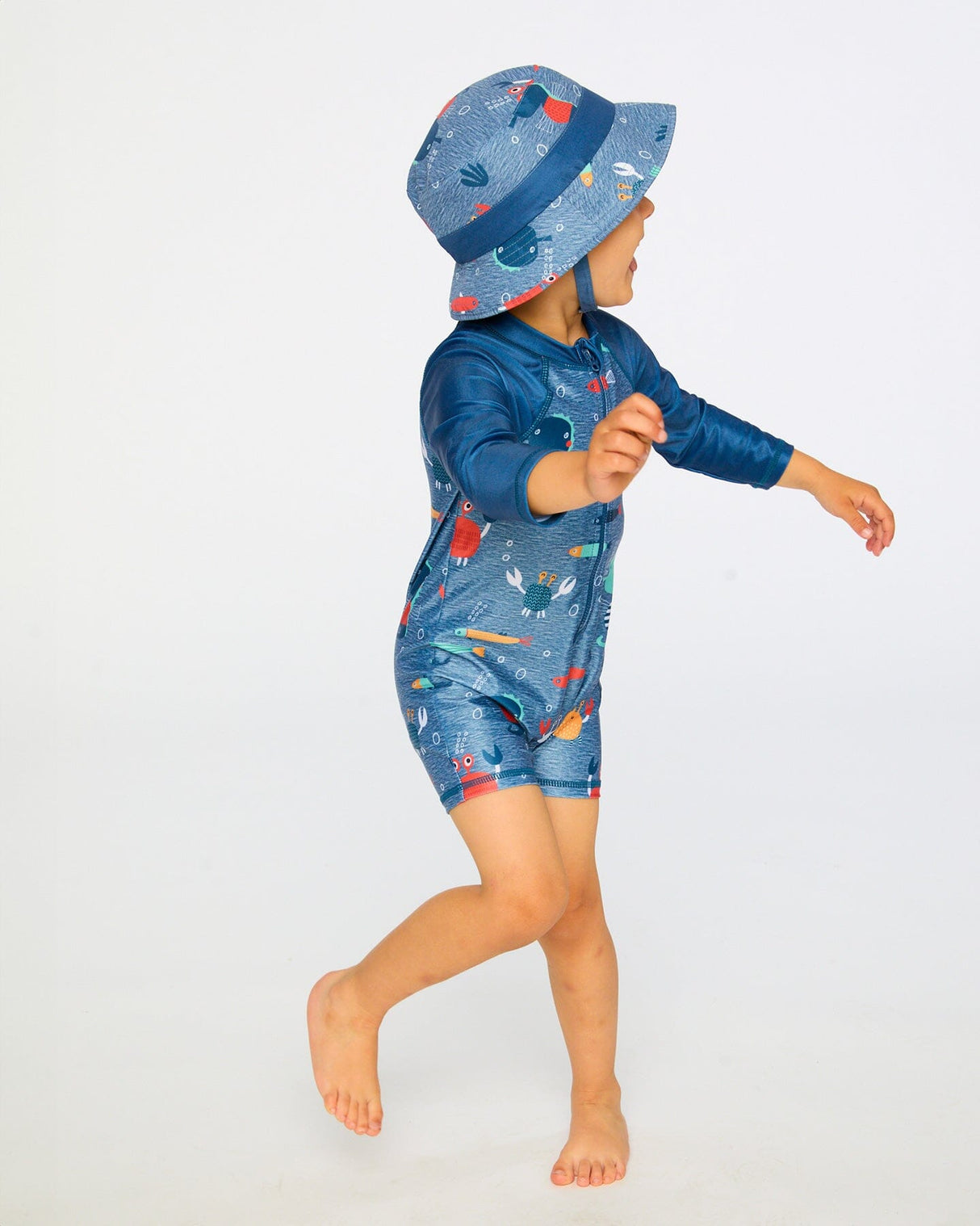 Toddler boy walking in side view wearing blue marine animals long sleeve rashguard swimsuit