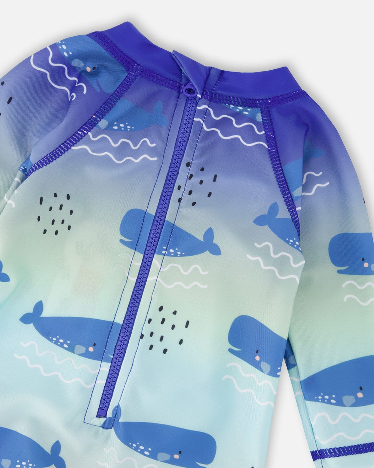 Detail shot of zipper, neckline, and whale pattern on blue rashguard swimsuit
