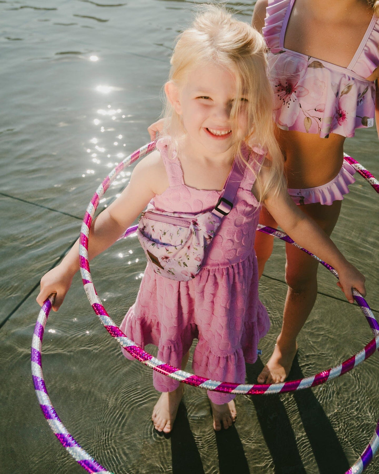 Girl standing in water wearing pink beach cover-up dress over swimsuit holding a hoop