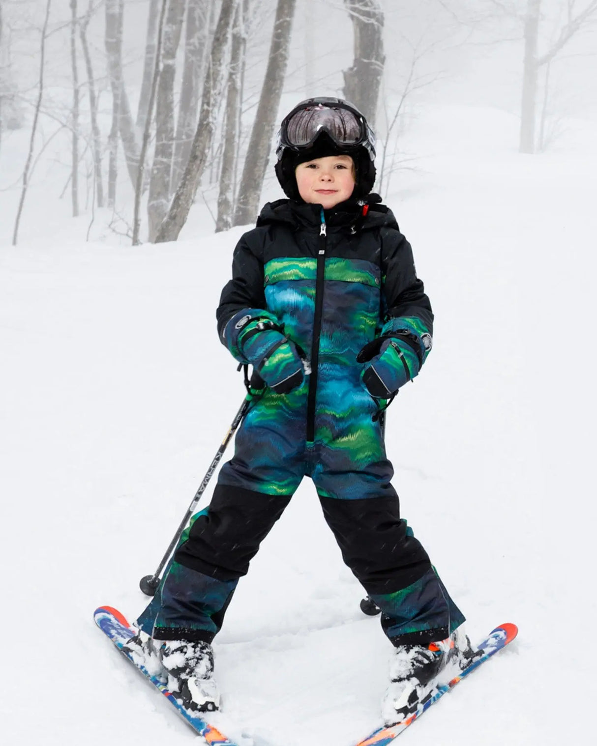 Child wearing Aurora Borealis one-piece Teknik snowsuit – front on snow