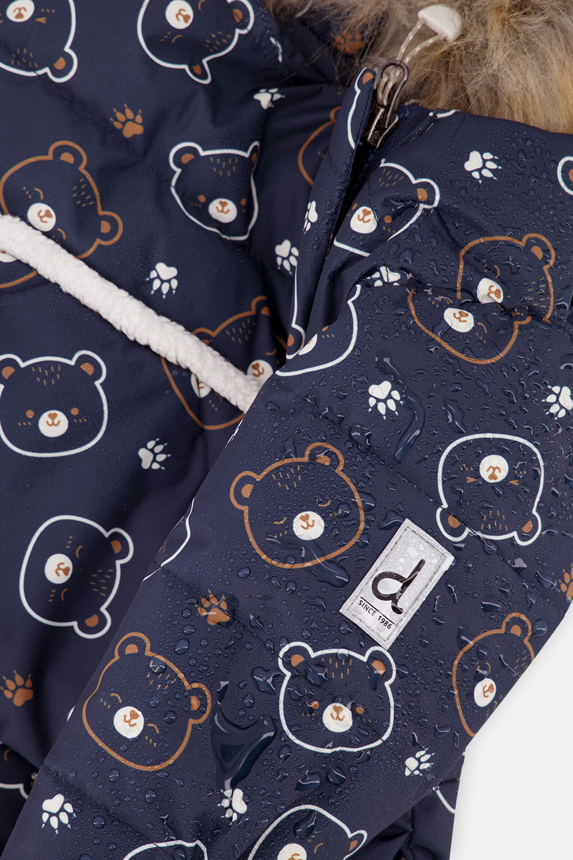 Close-up of the navy teddy bear print and logo tab on the Baby Snug snowsuit