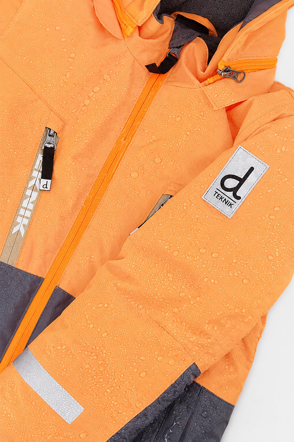 Water beading on the orange and grey TEKNIK jacket shell beside the logo patch