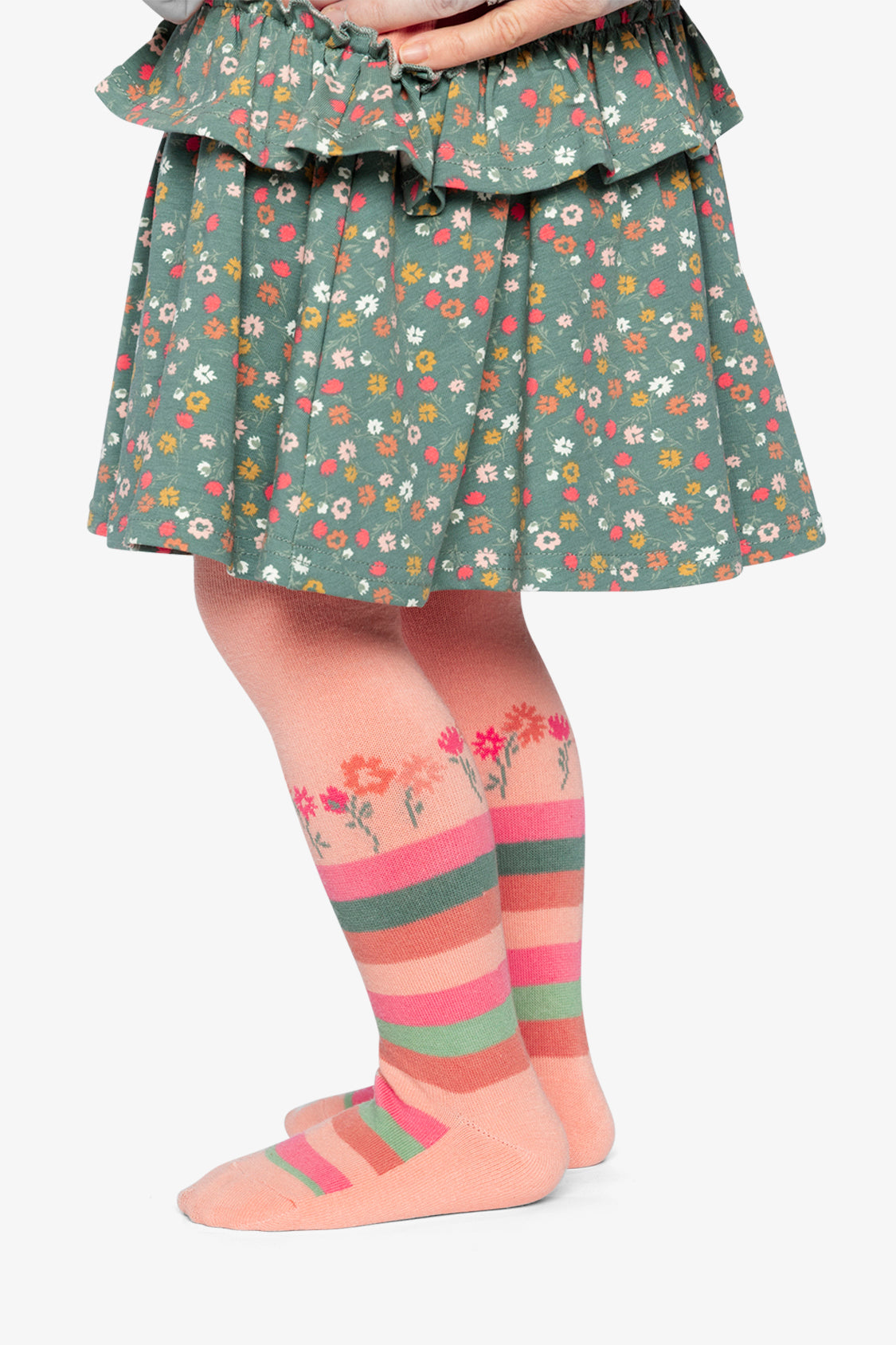 Child wearing the peach-pink striped ankle tights with a floral skirt, side view
