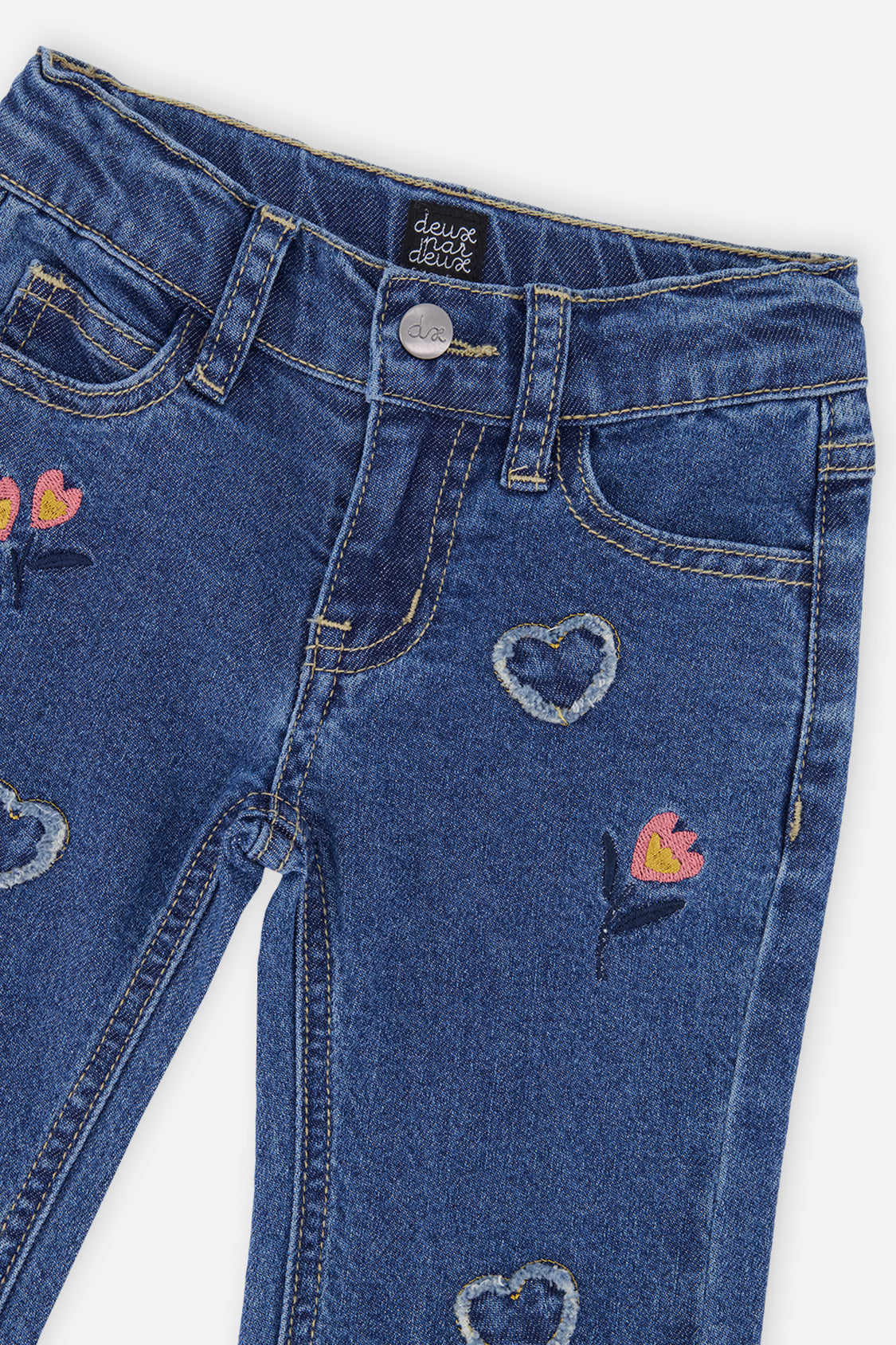 Close-up of the waist button, belt loops and embroidered hearts and flowers on the navy jeans