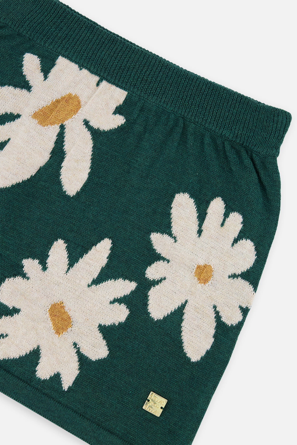 Close-up of the ribbed waistband and oversized daisy jacquard print on the green knitted skirt