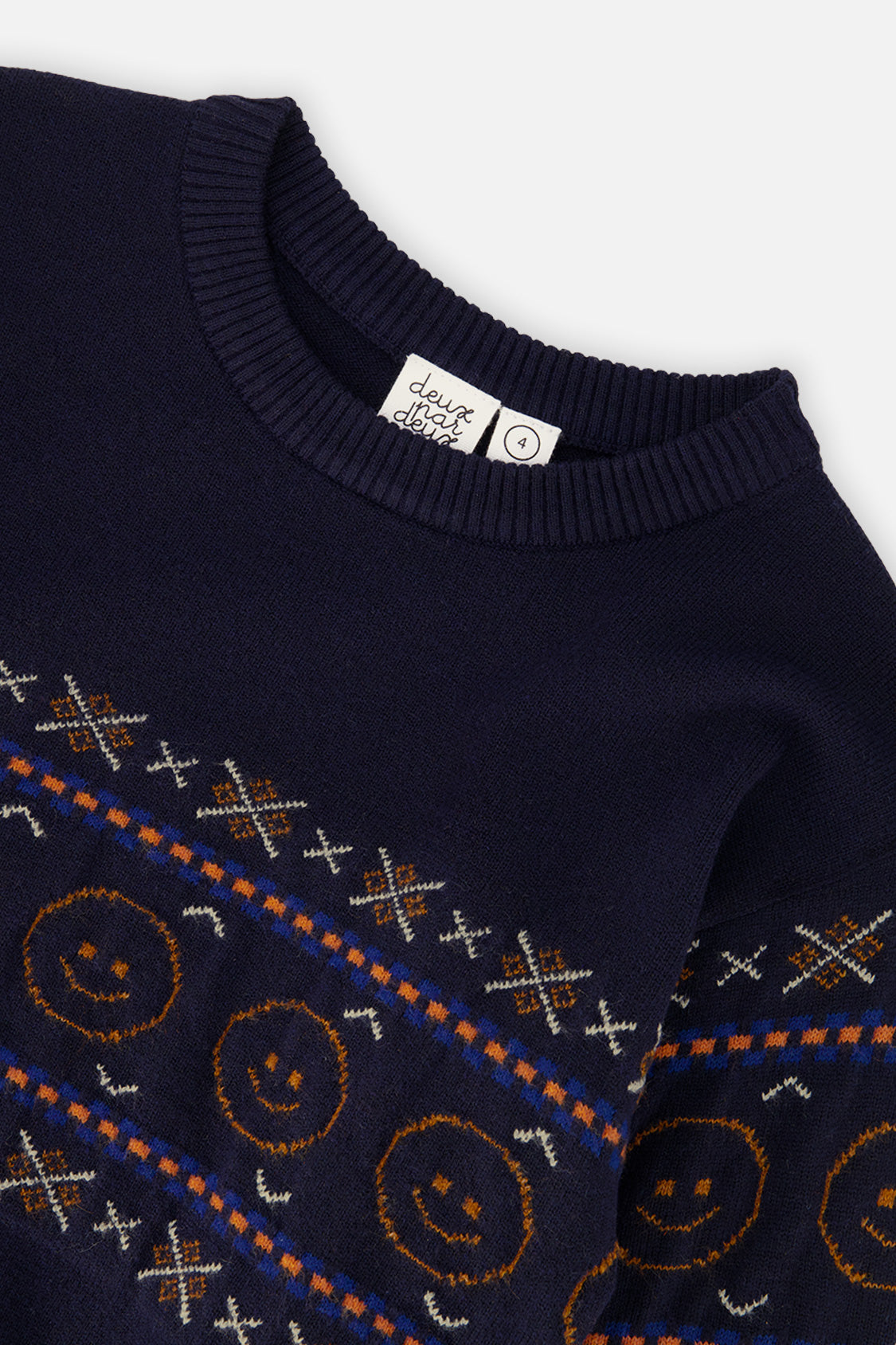 Close-up of the orange smiley faces and cross motifs on the dark blue Deux par Deux sweater