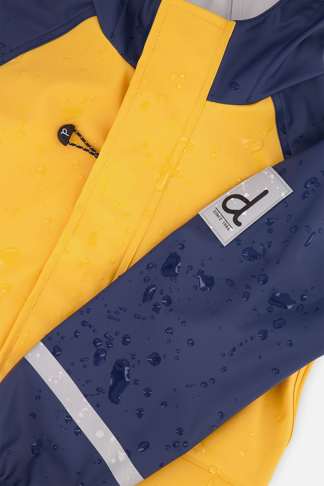 Close-up of the sleeve label, drawcord toggle and reflective sleeve stripe on the yellow and navy Deux par Deux rain jacket