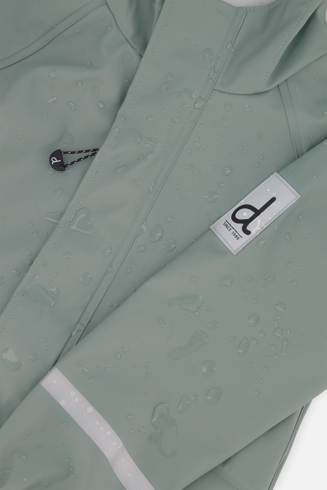 Close-up of the sage green rain jacket sleeve with the Deux par Deux label and reflective band