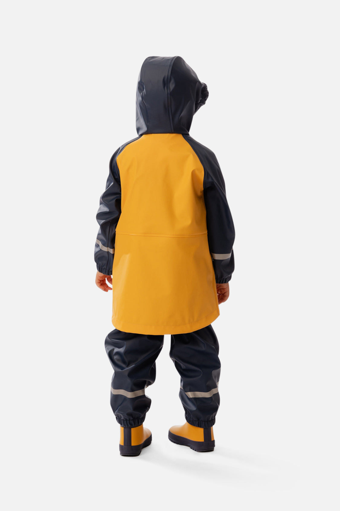 Child wearing the yellow and navy Deux par Deux rain jacket with navy rain pants and yellow boots, back view