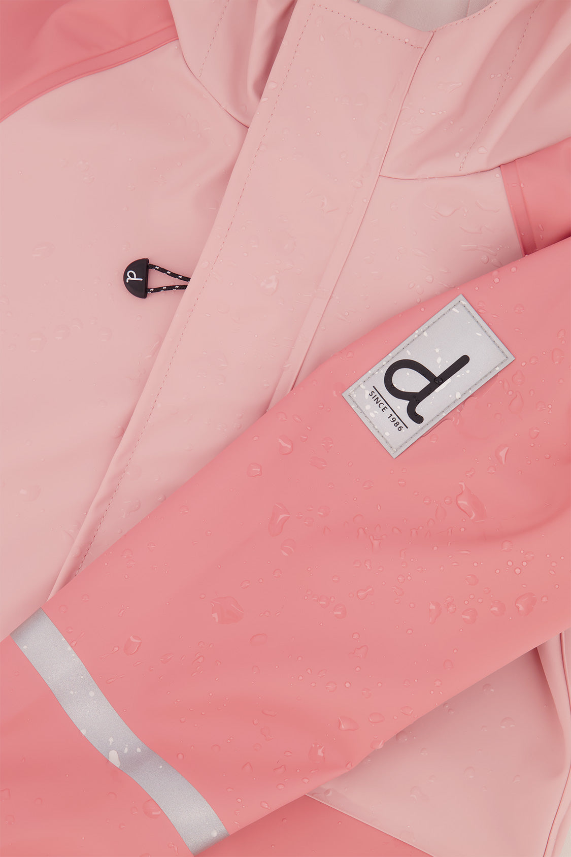 Close-up of the Deux par Deux label and reflective band on the pink rain jacket sleeve