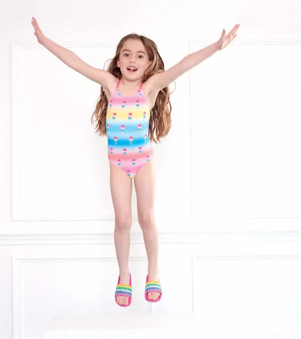 Girl jumping in Hatley Sweet Treats multicolor girls one-piece swimsuit with pastel stripes and treats print