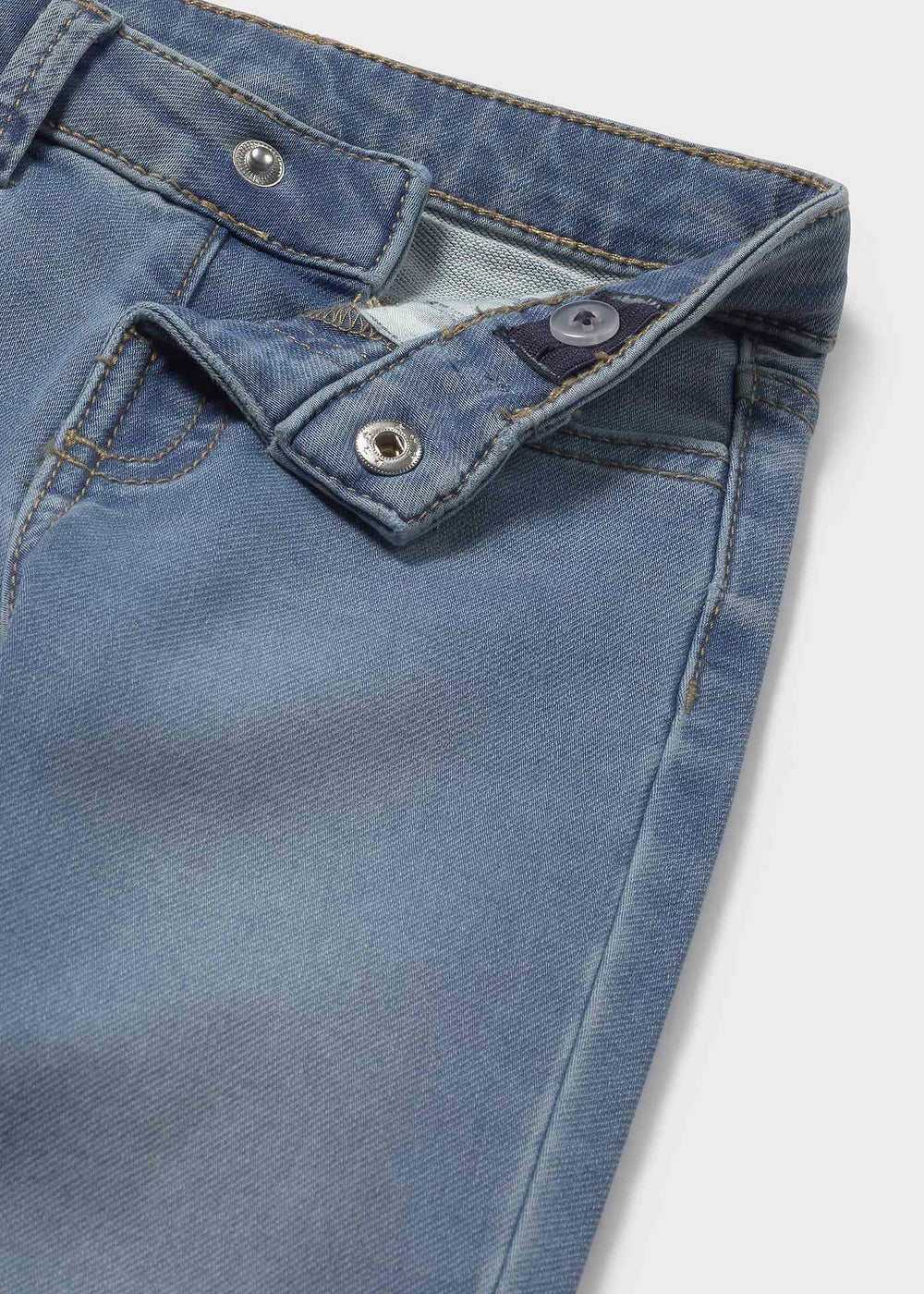Closeup of button, simulated fly and inner elastic on Mayoral baby jeans; soft light-wash denim texture.