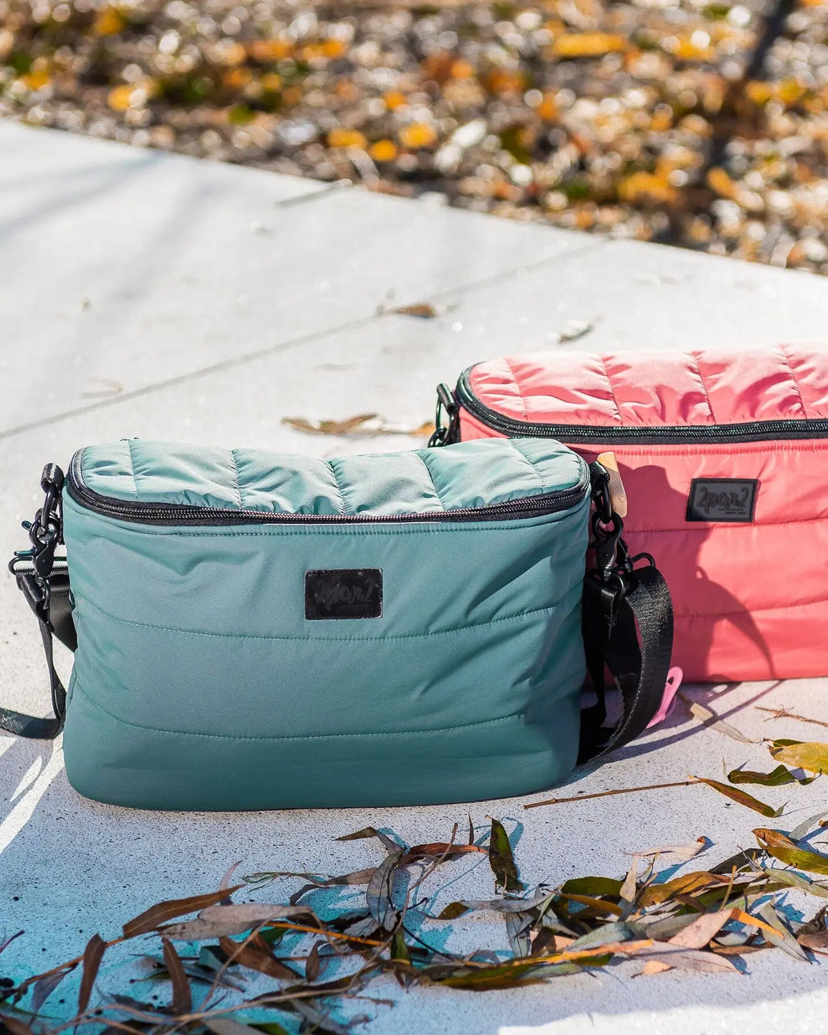 Sage green and coral quilted mini diaper bags sitting on a sunny stone ledge