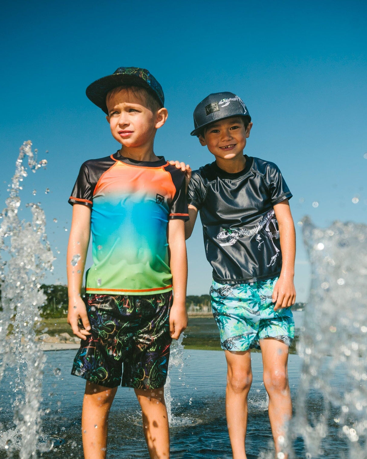 Two boys wearing gradient kids rashguard and matching swim trunks standing on the beach