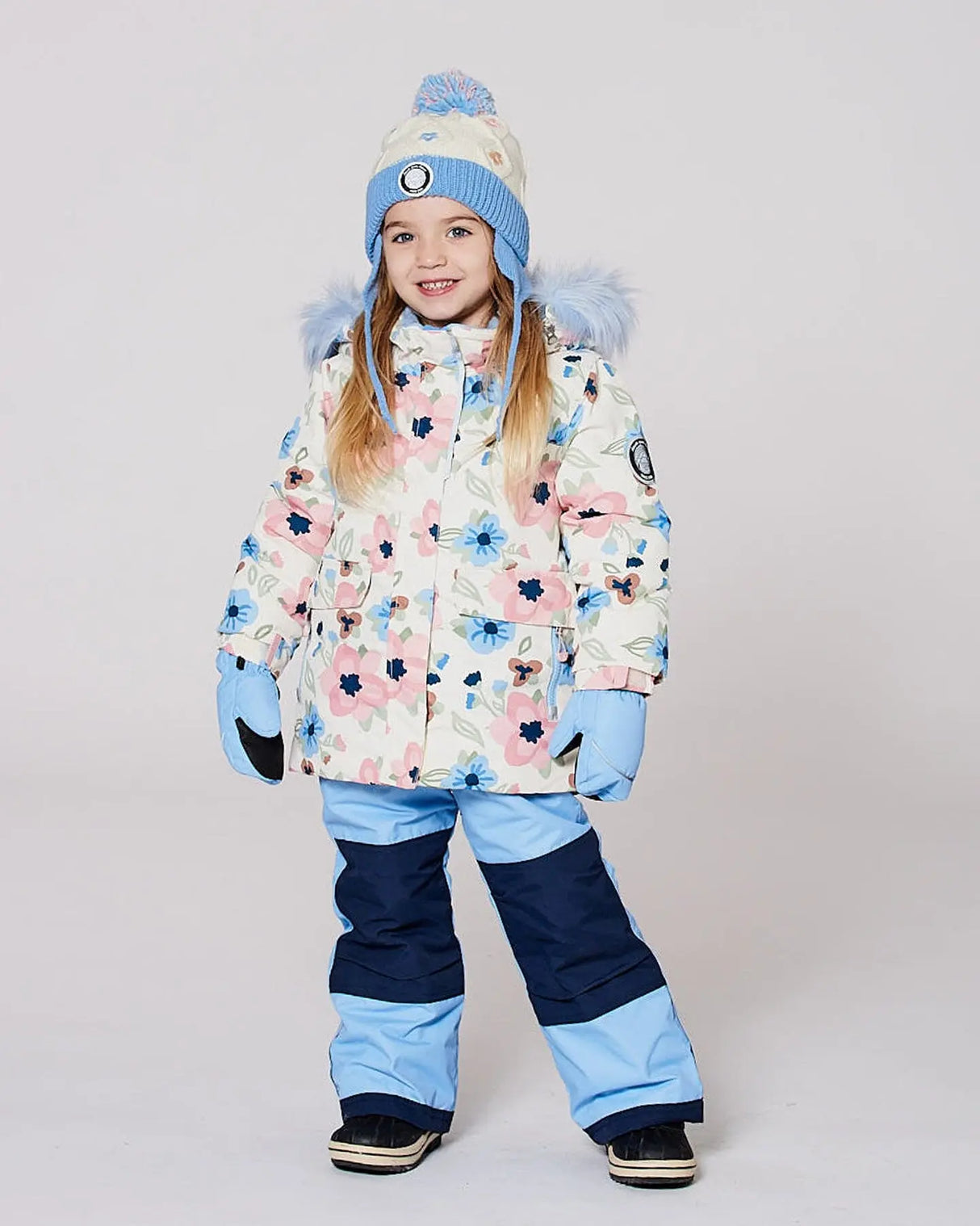 Girl wearing light-blue jacket and snow pants with adjustable suspenders.