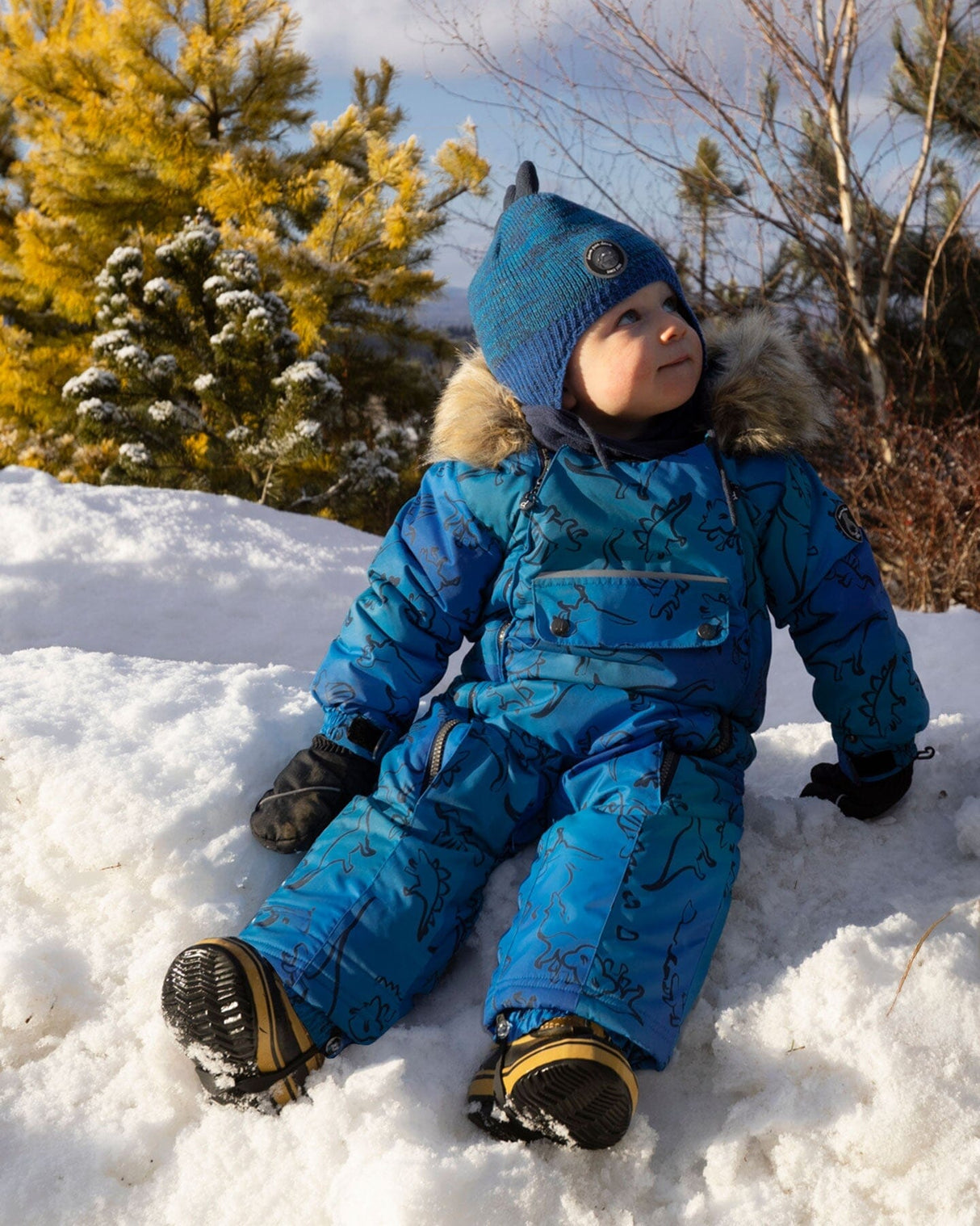 Lifestyle photo of toddler wearing the Deux par Deux blue dinosaur snowsuit outdoors