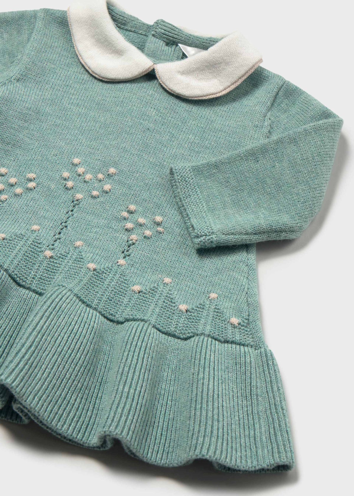 Close-up of the cream collar, dotted flower-stem knit pattern and ribbed ruffle hem on the sage green dress