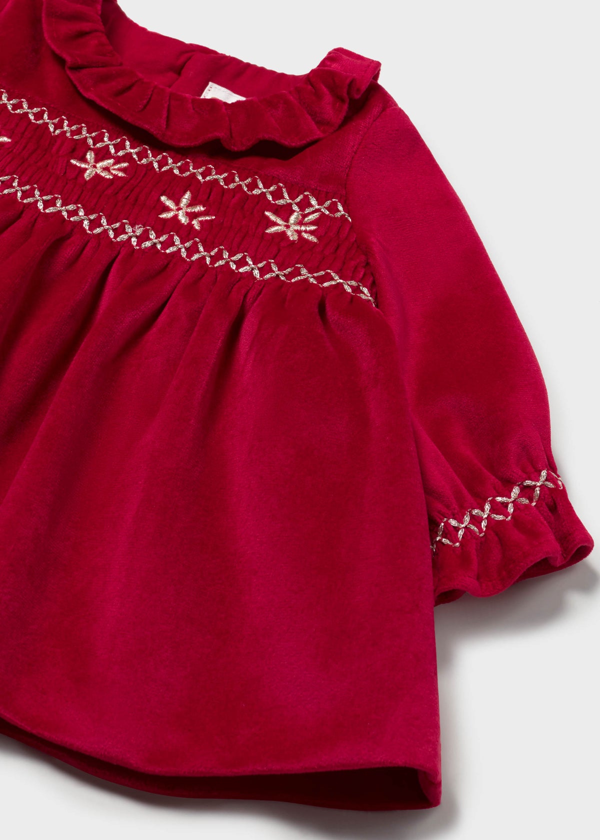 Close-up of the gold-tone embroidered honeycomb smocking and ruffled cuff on the red velvet dress