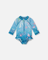 Front flat lay of Deux par Deux baby girl long sleeve rashguard one-piece in blue shell print