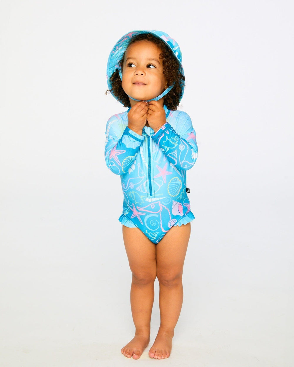 Toddler girl wearing blue shell print one-piece swimsuit front view with ruffle legs