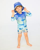 Toddler boy standing in blue whale long sleeve rashguard swimsuit front view