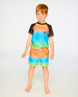 Boy wearing gradient boys swim trunks and rashguard, standing front view
