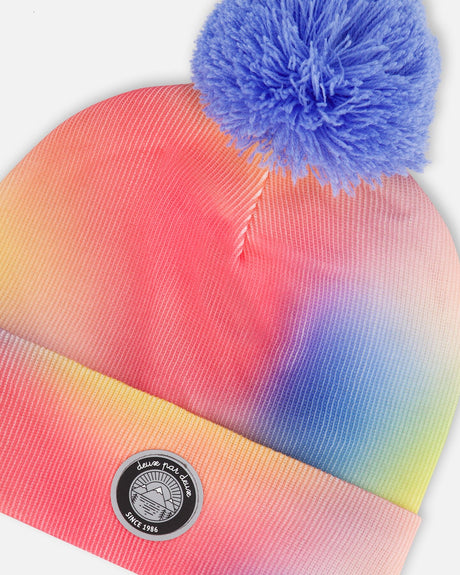 Close-up of the coral yellow and blue watercolor print round badge and pompom on the Deux par Deux hat