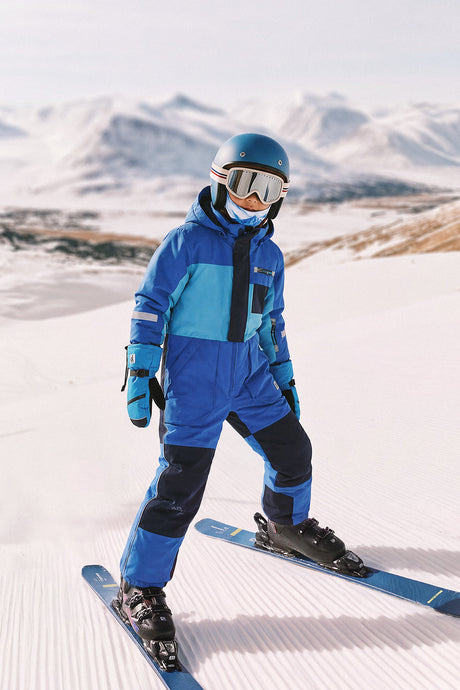 Child skiing in the Deux par Deux PLAY one-piece snowsuit in light and dark blue