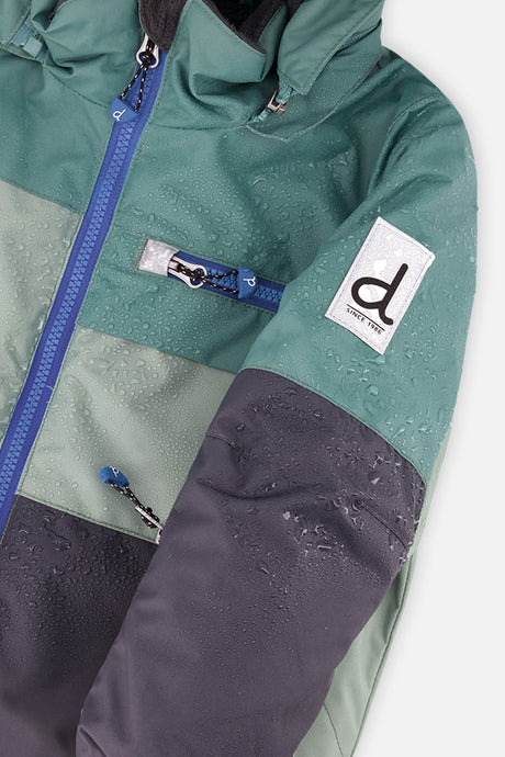 Close-up of the green and navy PLAY jacket front zipper, chest pocket and sleeve logo patch