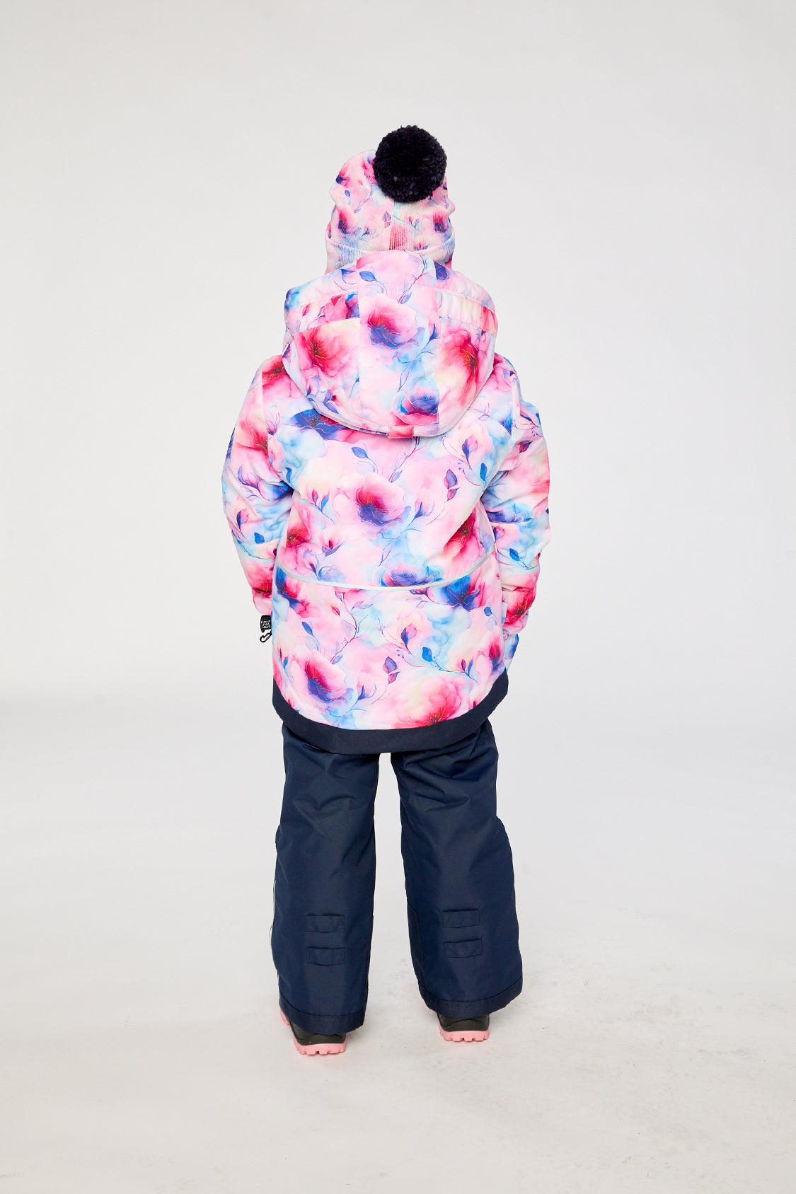Child wearing the mauve floral PLAY snowsuit with navy pants, back view