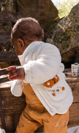 Baby wearing the off-white Deux par Deux sherpa jacket with bunny pocket, side view outdoors