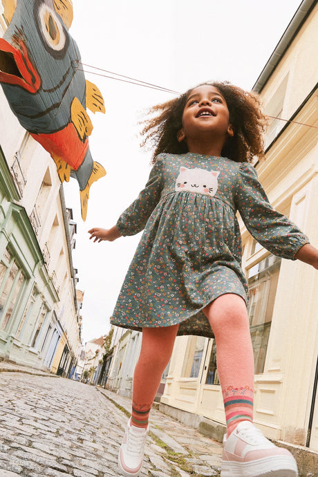 Child wearing the peach-pink striped ankle tights with a floral dress while walking along a cobbled street
