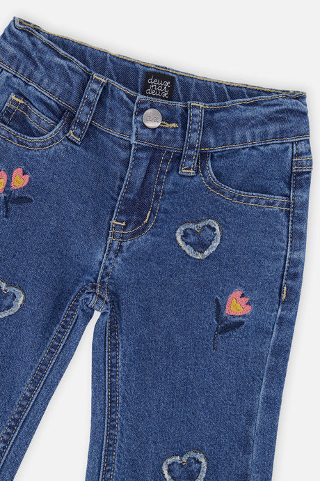 Close-up of the waist button, belt loops and embroidered hearts and flowers on the navy jeans