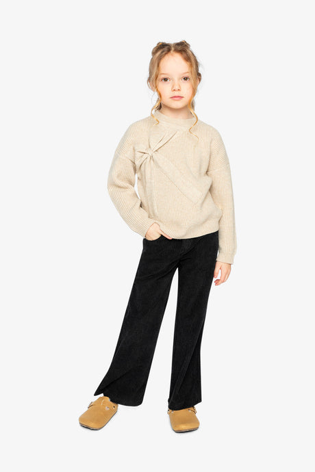 Child wearing the beige Deux par Deux bow sweater with black flared pants and tan shoes, full length view