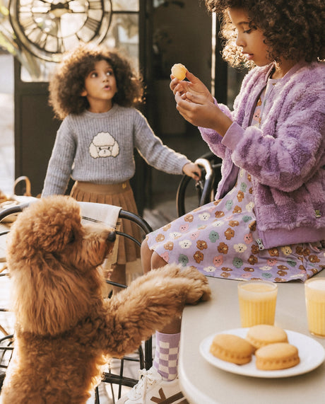 Two children at a cafe table with a brown poodle, one wearing a lilac plush jacket