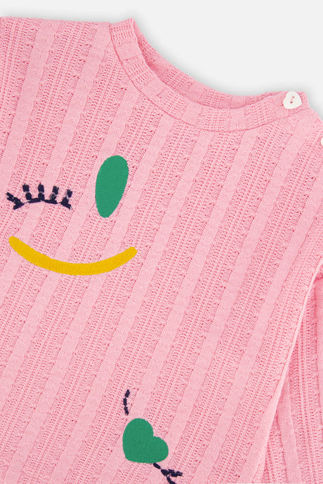 Close-up of the shoulder button, crew neckline and winking face motif on the pink knit top