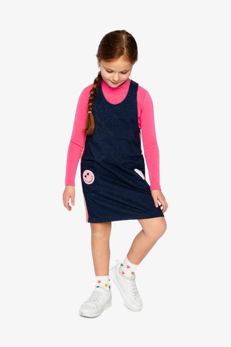 Child wearing the Deux par Deux navy overall dress over a pink turtleneck