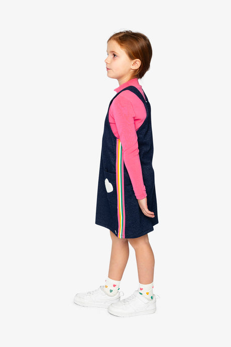 Child wearing the Deux par Deux navy overall dress, side view with rainbow stripe