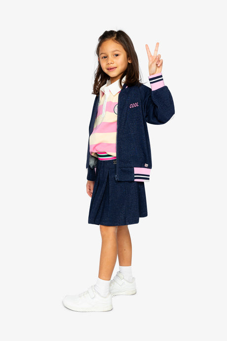 Child wearing the navy French terry bomber jacket with a navy skirt and white sneakers, full-length view