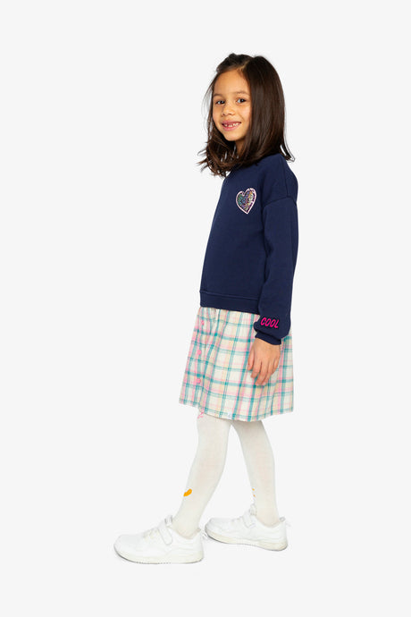 Child wearing the Deux par Deux navy sweatshirt dress with a plaid skirt, side view
