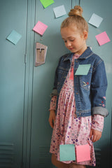 Child wearing the blue denim jacket over a floral dress in front of school lockers
