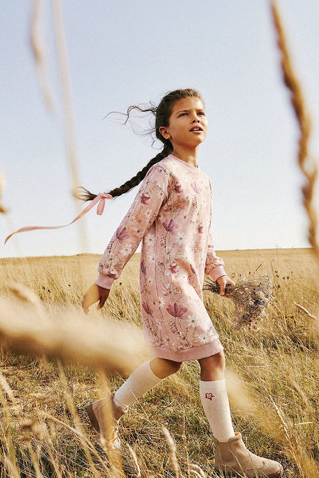 Child walking through tall grass in the Deux par Deux pink flower print dress with cream knee socks