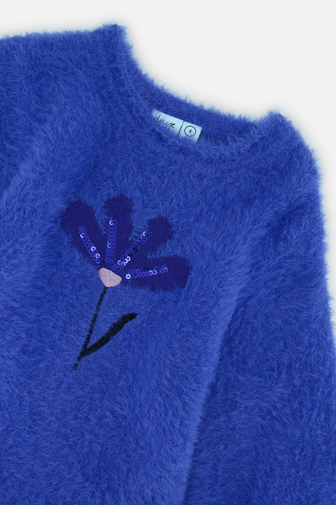 Close-up of the sequin flower on the fuzzy royal blue knit