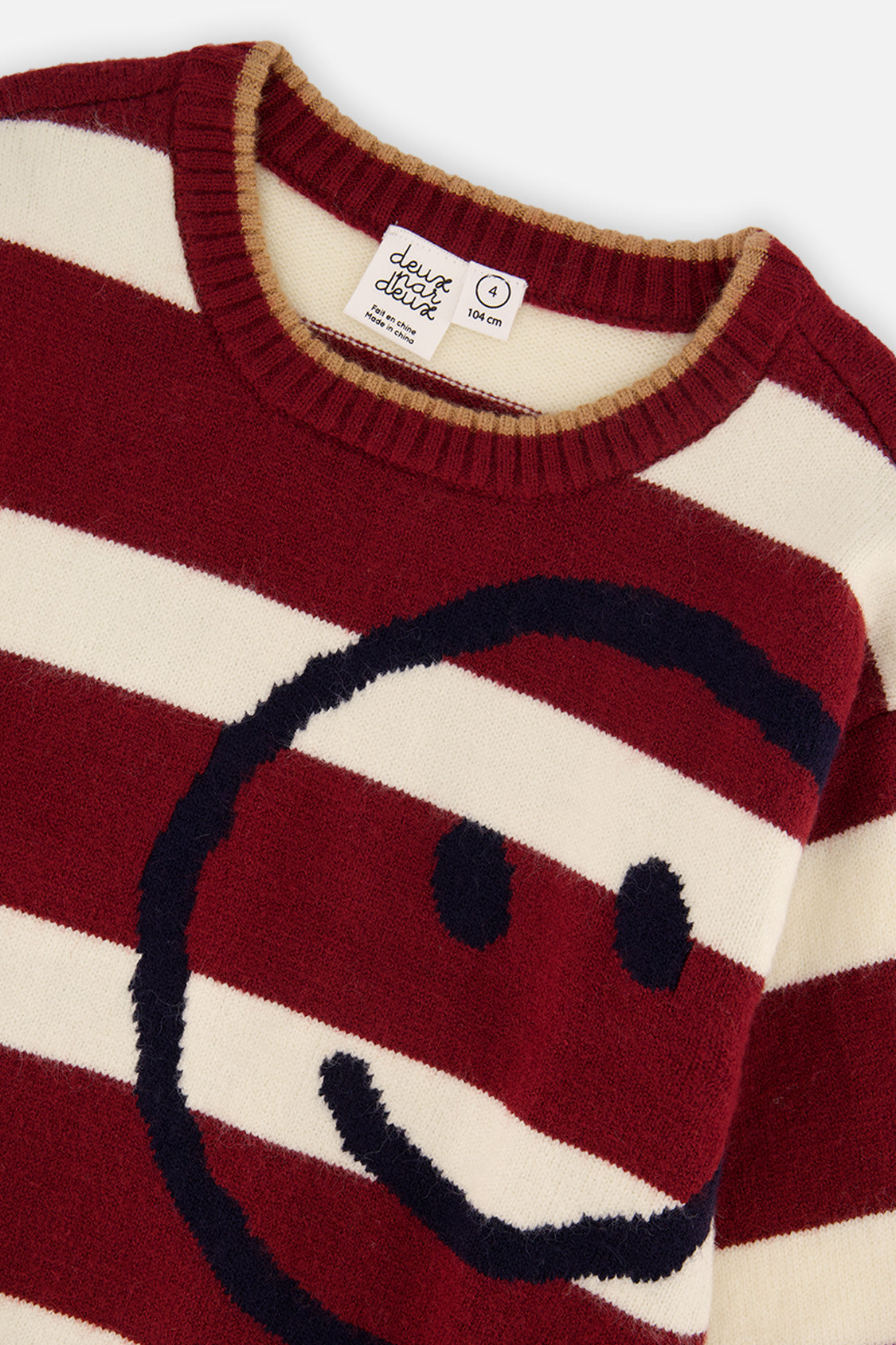 Close-up of the textured navy smiley face and tan-trimmed ribbed neckline on the burgundy and cream striped Deux par Deux sweater