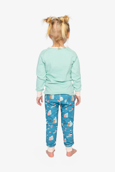 Back view of a child in the plain mint pajama top and blue pants printed with mountains and little houses