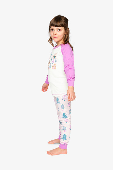 Child wearing the pink tree print pajama set in a side view with the gingerbread house print on the chest