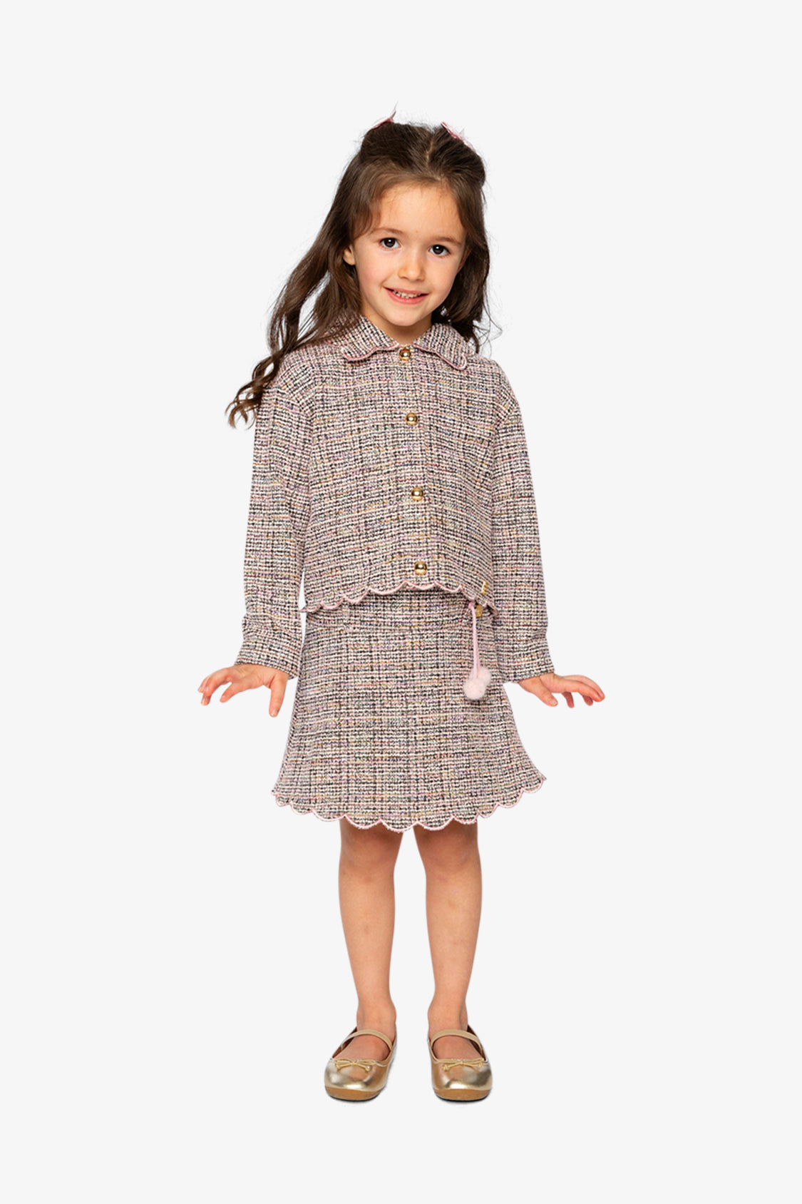 Child wearing the pink and black Deux par Deux cropped jacket with a skirt and gold shoes, full length view