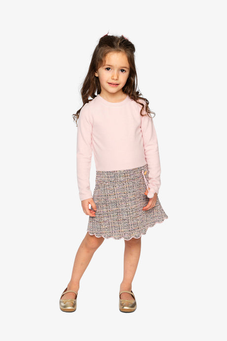 Child wearing the pink and black knit dress with a scalloped skirt hem, front view