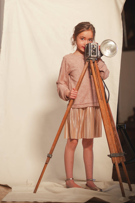 Child standing behind a vintage camera in the Deux par Deux dusty pink pleated dress