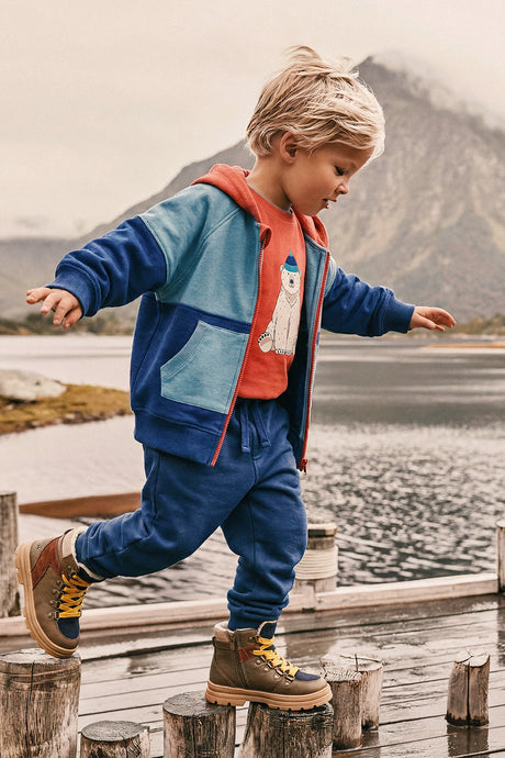 Child wearing the rose orange polar bear tee under a blue zip hoodie while walking on a lakeside dock